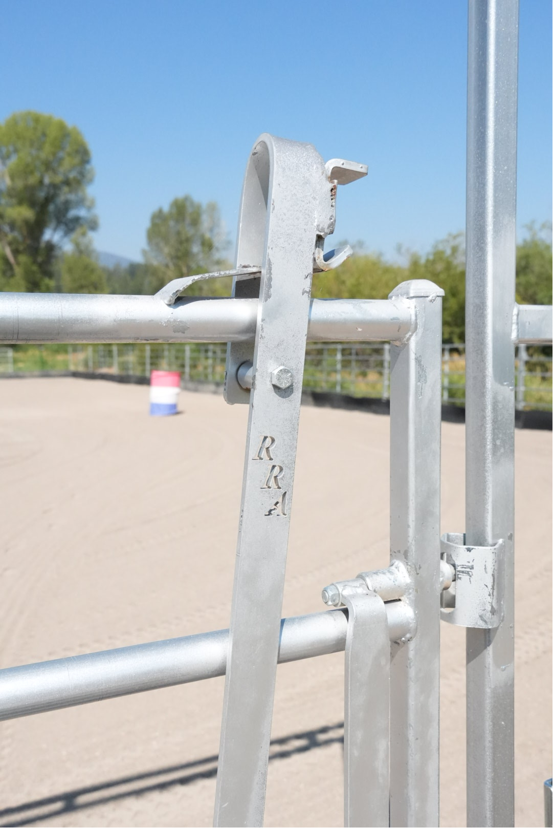Close-up of the RRA-branded latch and long handle on a galvanized Red River Arenas walk-thru gate