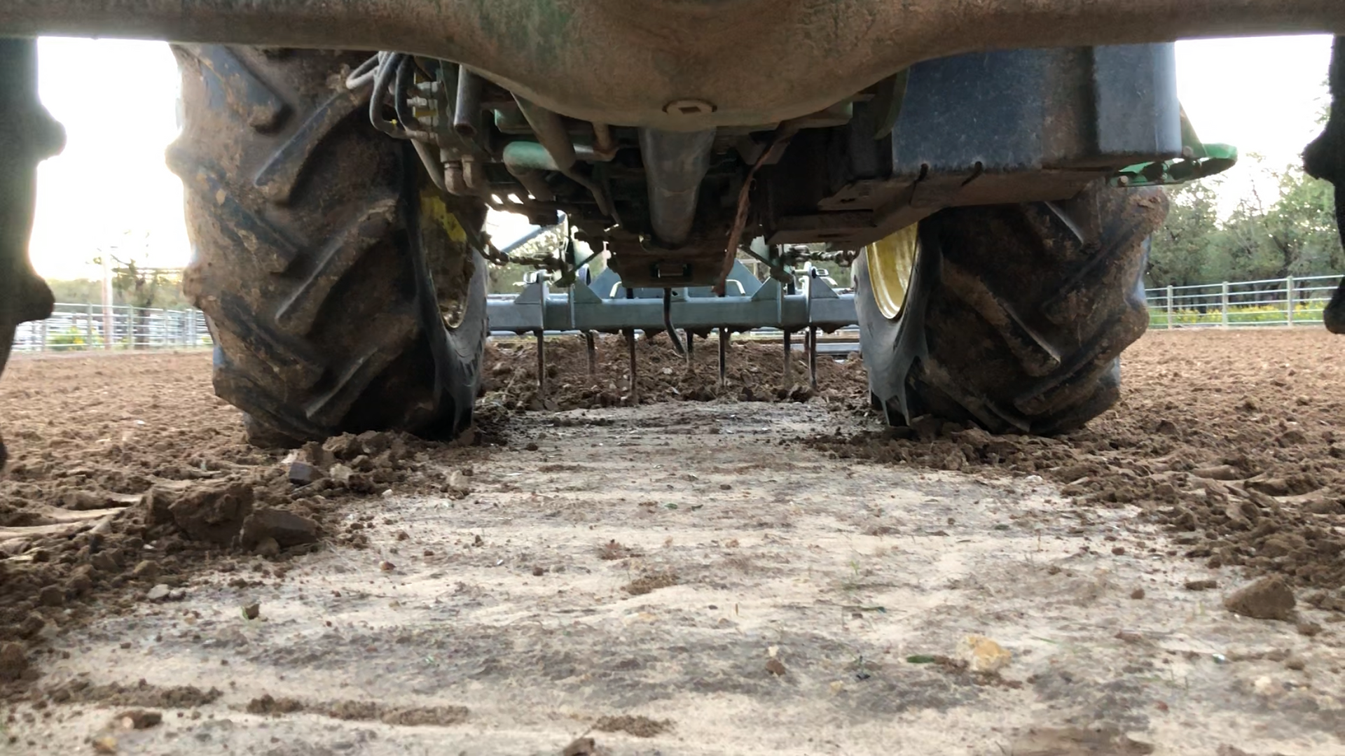 Ground-level view of Buster 2.0 arena groomer ripper shanks conditioning horse arena footing behind tractor